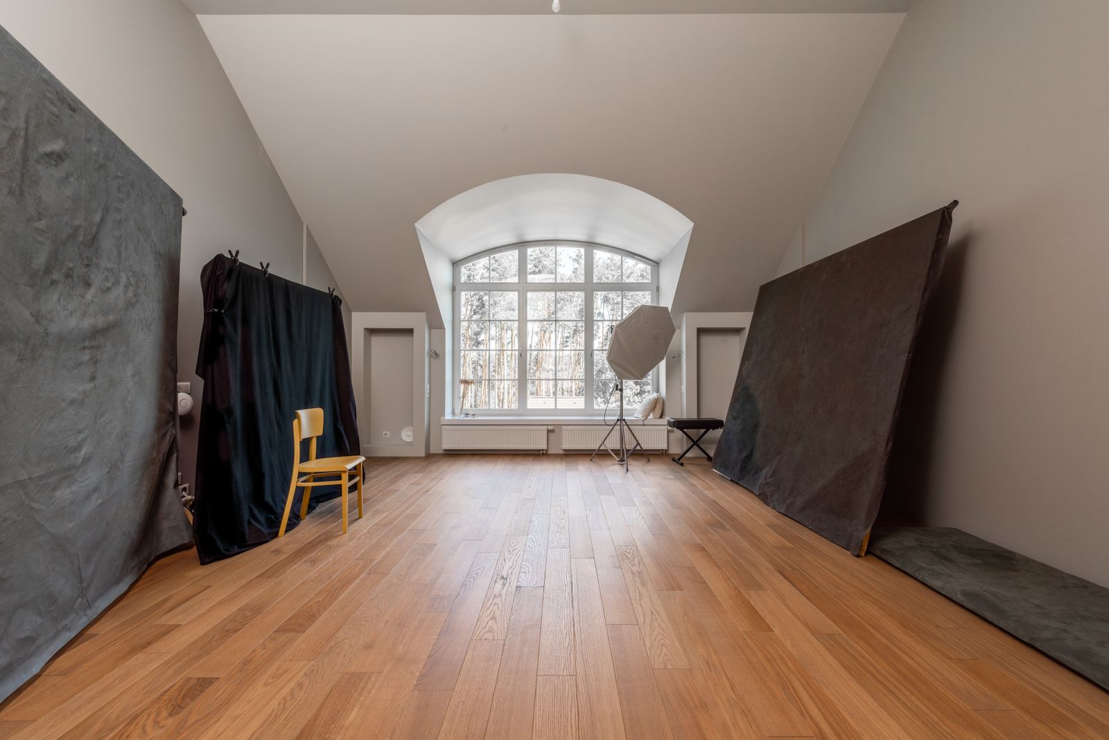 The Solarium, a vaulted studio room full of daylight, with an arched window and a warm wooden floor